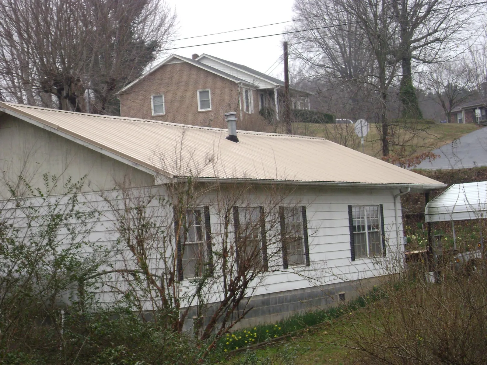 Tan metal roof on a white sided house set into a hillside — Commercial Roofing by Roofing Brothers in Broadview